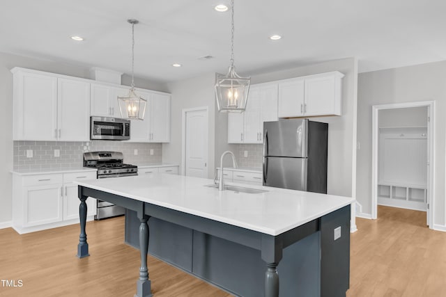 kitchen featuring appliances with stainless steel finishes, a sink, light wood finished floors, white cabinets, and recessed lighting