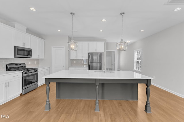 kitchen with stainless steel appliances, a sink, light wood finished floors, decorative backsplash, and white cabinetry