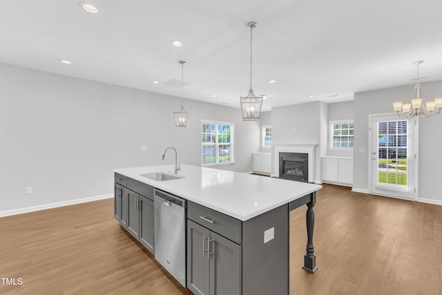 kitchen featuring stainless steel dishwasher, a sink, gray cabinetry, a chandelier, and light wood-style floors