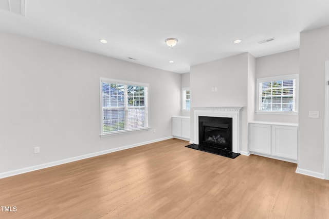 unfurnished living room with light wood finished floors, healthy amount of natural light, baseboards, a fireplace with raised hearth, and recessed lighting