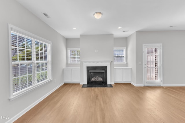 unfurnished living room with light wood-type flooring, baseboards, a fireplace with raised hearth, and recessed lighting