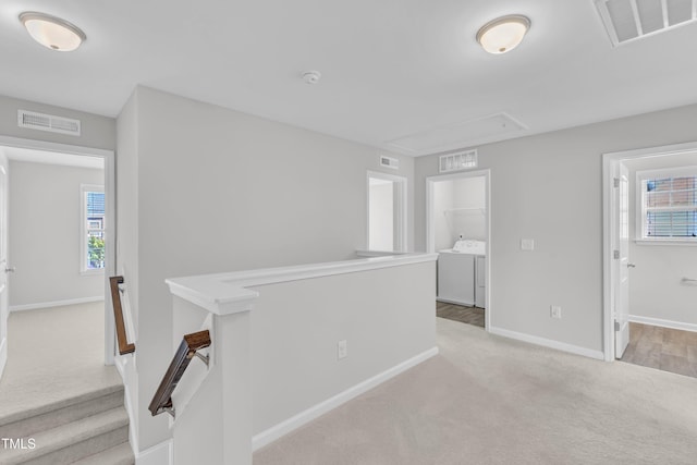hallway with attic access, an upstairs landing, carpet floors, baseboards, and independent washer and dryer
