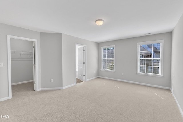 unfurnished bedroom with a spacious closet, baseboards, light colored carpet, and a closet