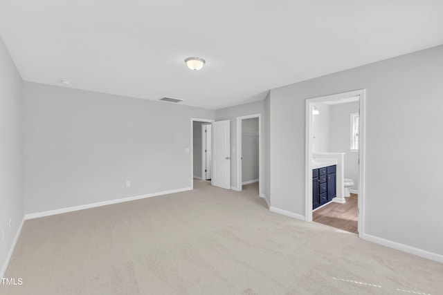 unfurnished bedroom with light colored carpet, baseboards, and ensuite bathroom