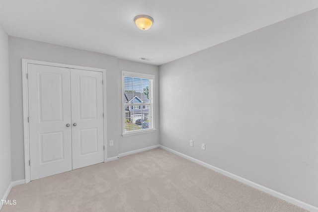 unfurnished bedroom featuring light colored carpet, a closet, and baseboards