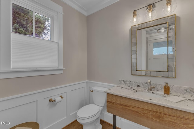 half bath featuring toilet, wood finished floors, healthy amount of natural light, a wainscoted wall, and vanity