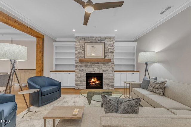 living room featuring ornamental molding, light wood-style flooring, ceiling fan, a stone fireplace, and built in features