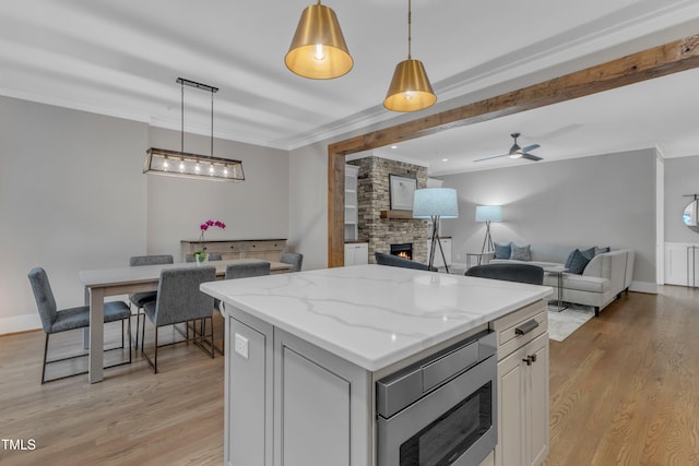 kitchen with stainless steel microwave, a fireplace, ornamental molding, light wood-style floors, and a kitchen island