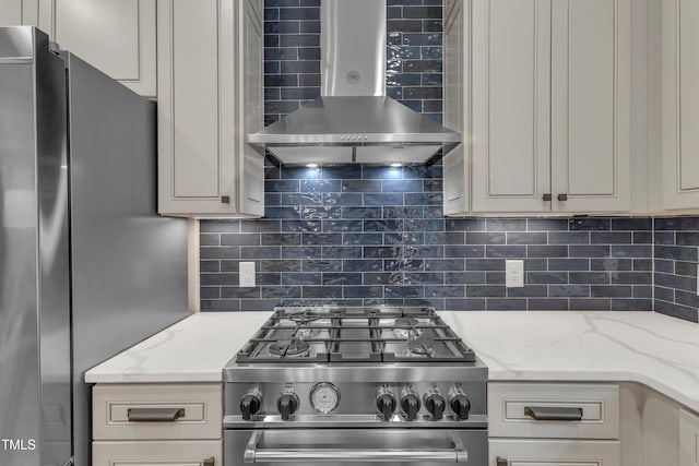 kitchen with appliances with stainless steel finishes, wall chimney range hood, decorative backsplash, and light stone counters