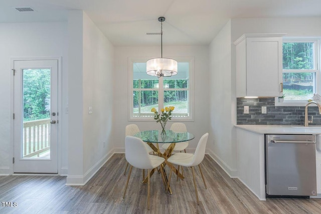 dining space featuring wood finished floors, visible vents, vaulted ceiling, a notable chandelier, and baseboards