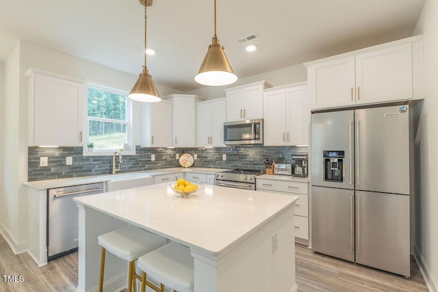 kitchen with white cabinetry, light wood-type flooring, stainless steel appliances, and backsplash