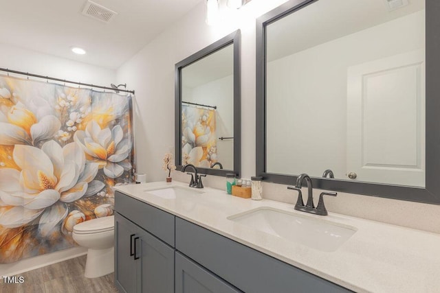 bathroom with toilet, visible vents, a sink, and wood finished floors