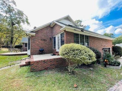view of side of home featuring a yard, a patio area, and brick siding