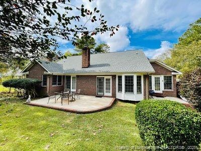 back of property with a yard, a patio area, brick siding, and a chimney