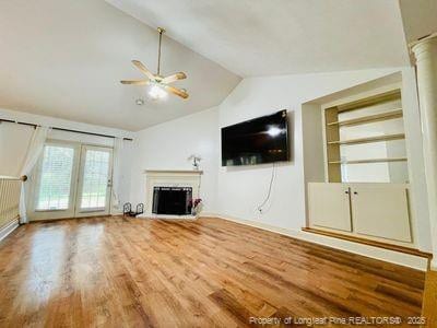 unfurnished living room featuring a fireplace with raised hearth, wood finished floors, lofted ceiling, and ceiling fan