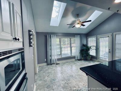 kitchen with a ceiling fan, baseboards, lofted ceiling with skylight, stainless steel microwave, and white cabinets