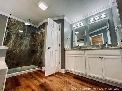 full bathroom featuring double vanity, a marble finish shower, wood finished floors, a sink, and ornamental molding