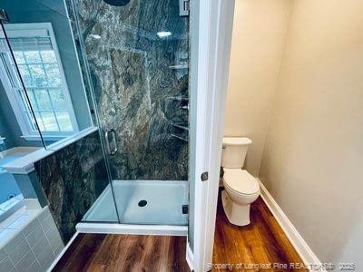 bathroom featuring a garden tub, toilet, wood finished floors, and a shower stall