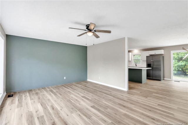 unfurnished living room featuring light wood finished floors, visible vents, baseboards, and a ceiling fan