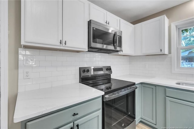 kitchen featuring backsplash, light stone countertops, white cabinetry, and appliances with stainless steel finishes