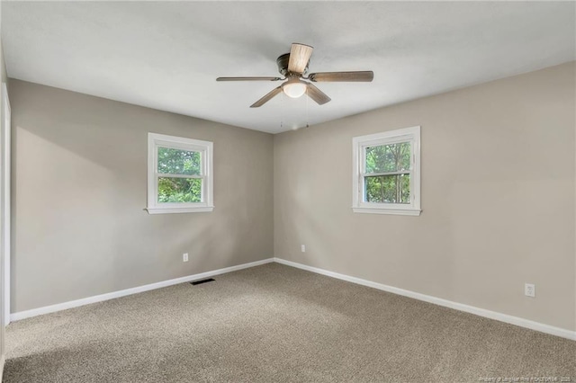carpeted empty room with baseboards, a ceiling fan, a healthy amount of sunlight, and visible vents