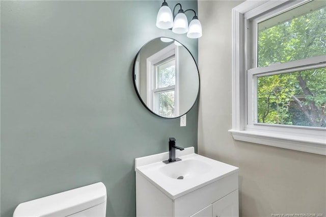half bath with toilet, an inviting chandelier, and vanity