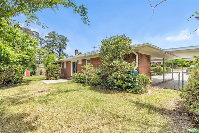 exterior space with fence, brick siding, a yard, a carport, and a chimney