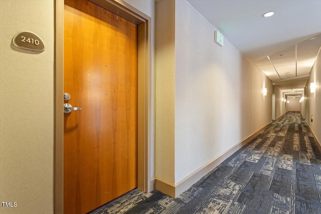 hall with carpet flooring, a drop ceiling, and baseboards