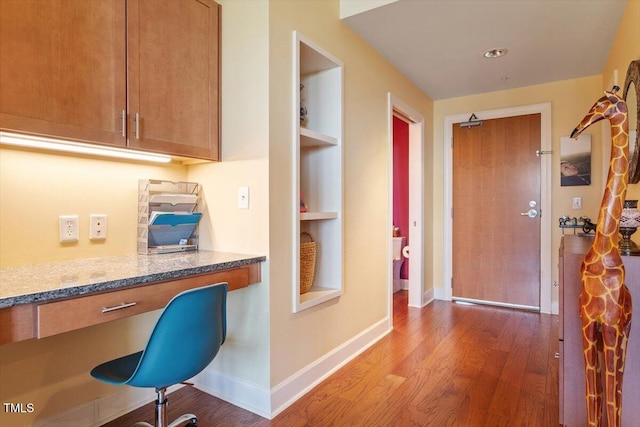 hallway featuring wood finished floors, baseboards, built in features, and an office area