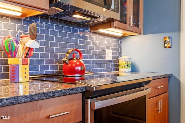 kitchen featuring stainless steel appliances, tasteful backsplash, brown cabinets, and glass insert cabinets
