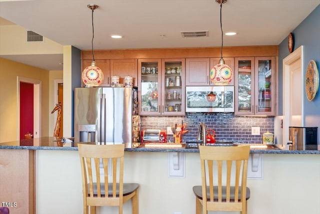 kitchen with appliances with stainless steel finishes, tasteful backsplash, brown cabinetry, glass insert cabinets, and recessed lighting