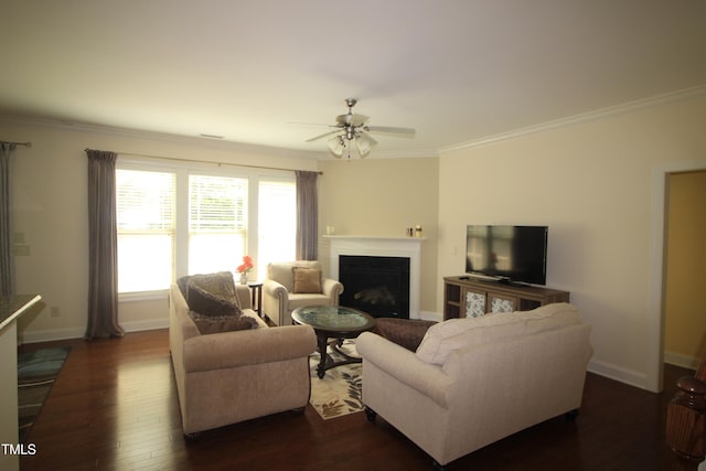 living area with dark wood-style flooring, a fireplace, ceiling fan, ornamental molding, and baseboards