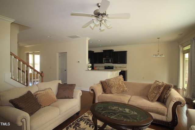 living area with ornamental molding, wood finished floors, a ceiling fan, stairway, and baseboards