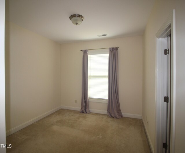 spare room featuring light colored carpet and baseboards