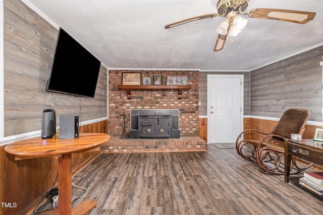 1169 Clayhole Rd, Dunn, NC 28334 - living room featuring wooden walls, a wood stove, wood finished floors, a ceiling fan, and wainscoting