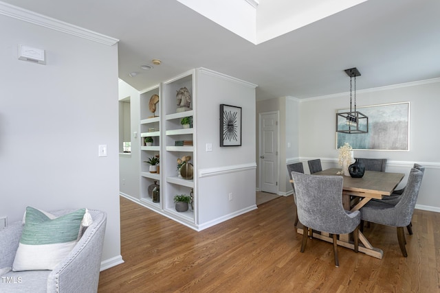 dining area featuring wood finished floors, crown molding, built in shelves, baseboards, and a chandelier