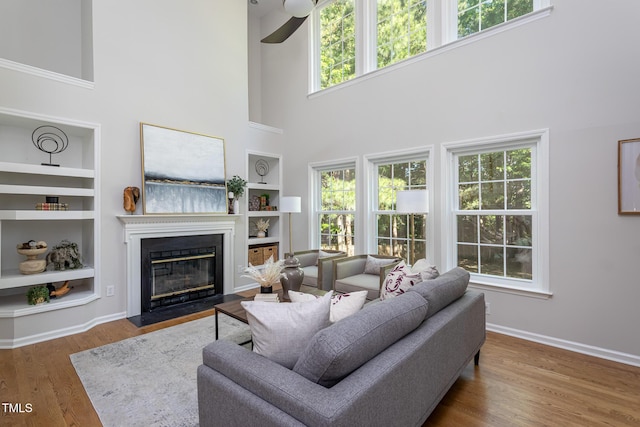 living area with built in features, a high ceiling, a fireplace with flush hearth, baseboards, and wood finished floors