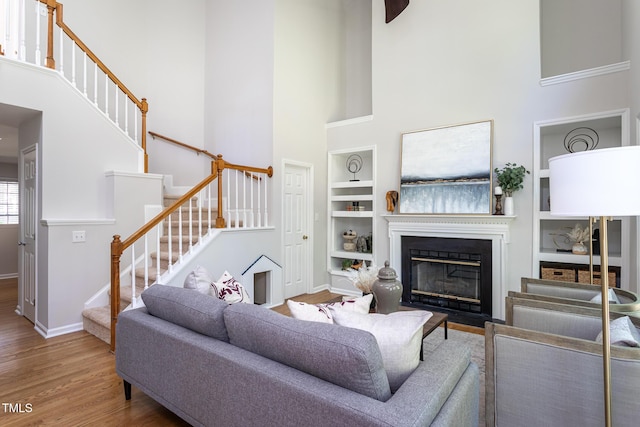 living room featuring a high ceiling, baseboards, built in features, stairs, and wood finished floors