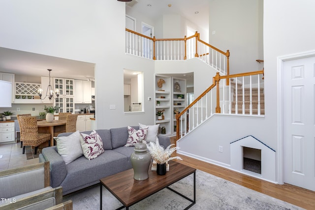 living area featuring stairs, a towering ceiling, light wood-type flooring, a chandelier, and baseboards