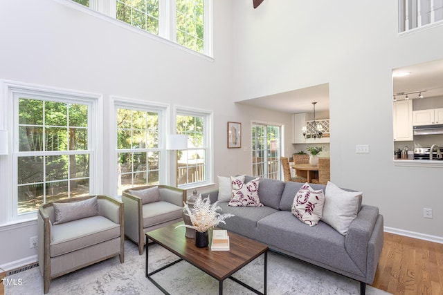 living area with light wood finished floors, plenty of natural light, a high ceiling, baseboards, and a chandelier