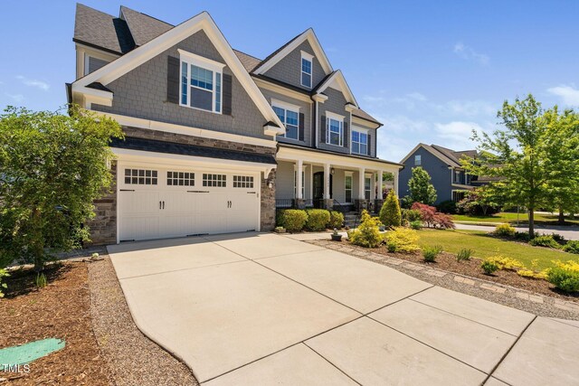 craftsman-style house featuring a porch, an attached garage, concrete driveway, stone siding, and a shingled roof