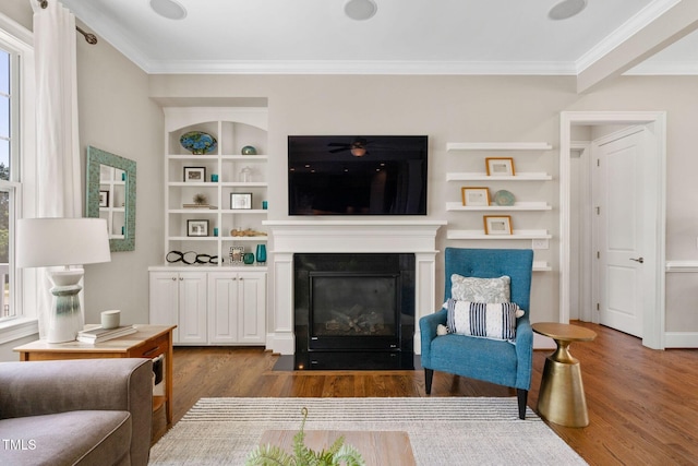 living area featuring wood finished floors, ornamental molding, a fireplace with flush hearth, and built in features