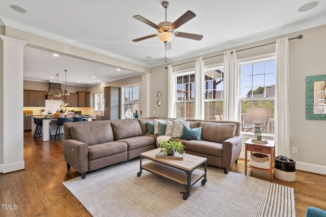 living room with decorative columns, ceiling fan, wood finished floors, ornamental molding, and baseboards