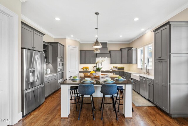 kitchen with stainless steel appliances, a sink, gray cabinets, custom exhaust hood, and a center island