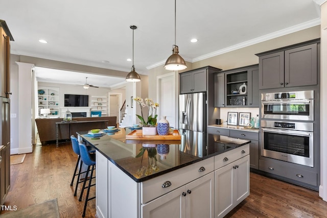 kitchen with stainless steel appliances, crown molding, dark stone counters, a ceiling fan, and dark wood finished floors
