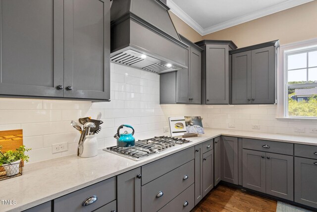 kitchen featuring gray cabinetry, stainless steel gas cooktop, premium range hood, ornamental molding, and decorative backsplash