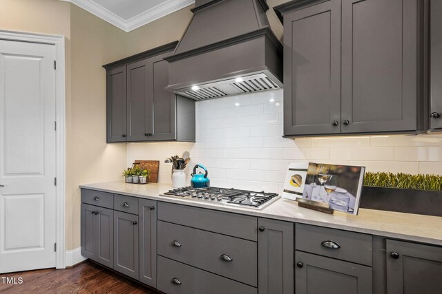 kitchen with custom range hood, stainless steel gas cooktop, gray cabinetry, crown molding, and backsplash