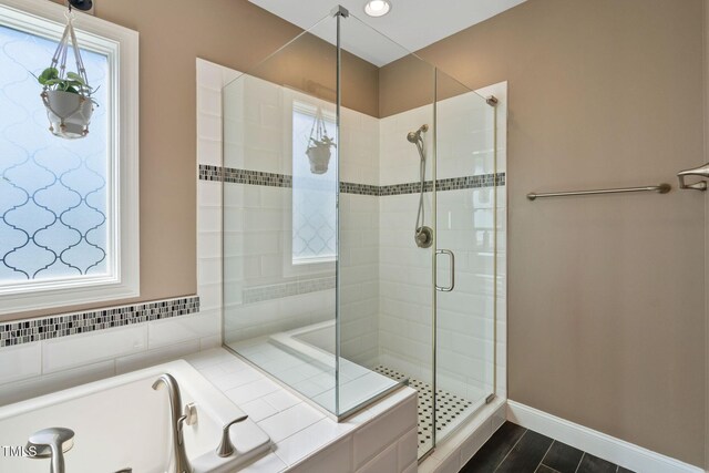 full bathroom with a shower stall, a bath, and baseboards