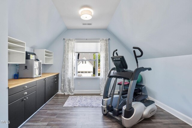 exercise room with dark wood-type flooring, vaulted ceiling, and baseboards
