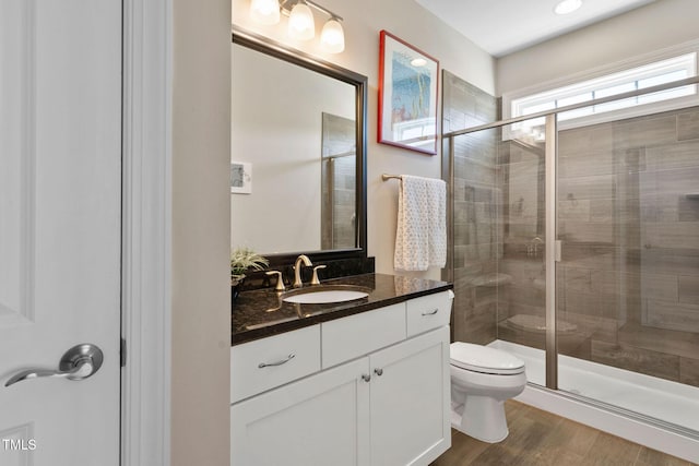 bathroom with a stall shower, toilet, vanity, and wood finished floors